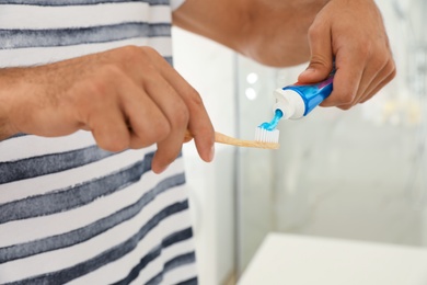 Man applying toothpaste on brush indoors, closeup