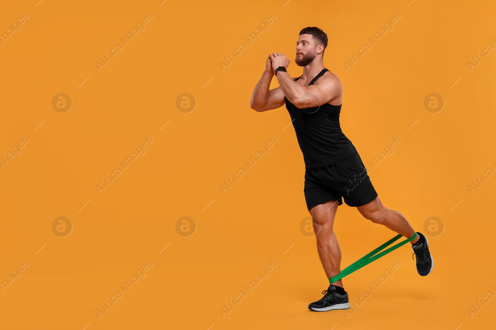 Photo of Young man exercising with elastic resistance band on orange background. Space for text