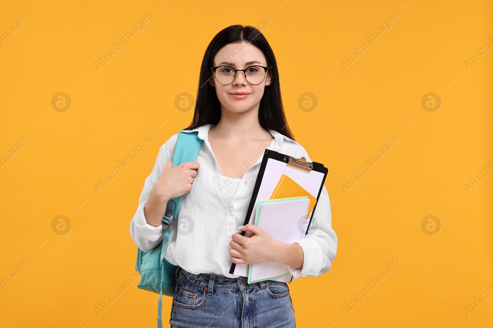 Photo of Student with notebooks and clipboard on yellow background