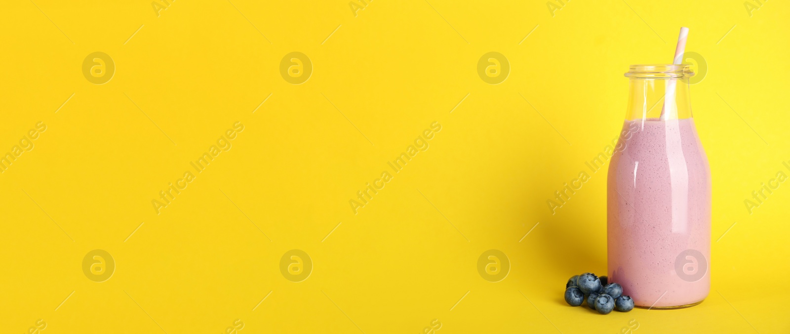 Photo of Tasty fresh milk shake and blueberries on yellow background. Space for text