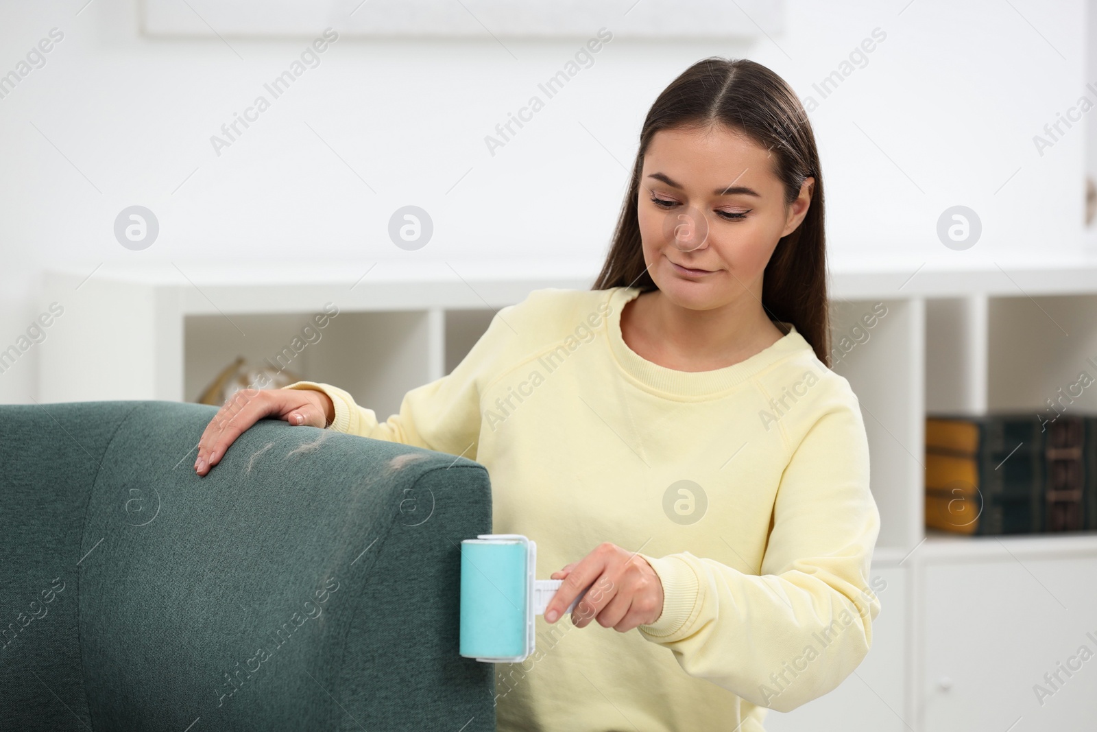 Photo of Woman with lint roller removing pet hair from sofa at home