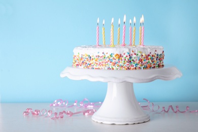 Photo of Birthday cake with burning candles on table against color background. Space for text