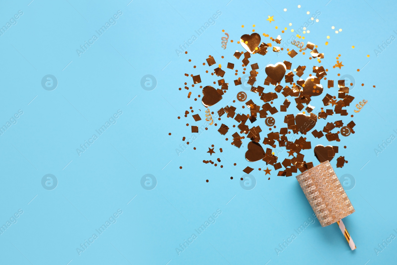 Photo of Shiny golden confetti bursting out of party cracker on light blue background, top view. Space for text