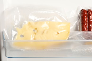 Photo of Vacuum bags with cheese and sausages in fridge, closeup. Food storage
