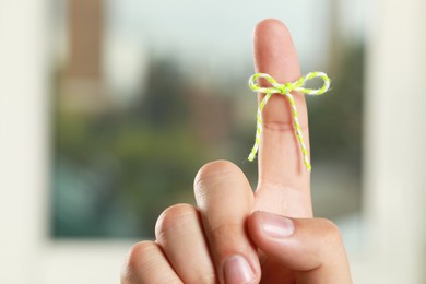 Man showing index finger with tied bow as reminder near window on blurred background, closeup