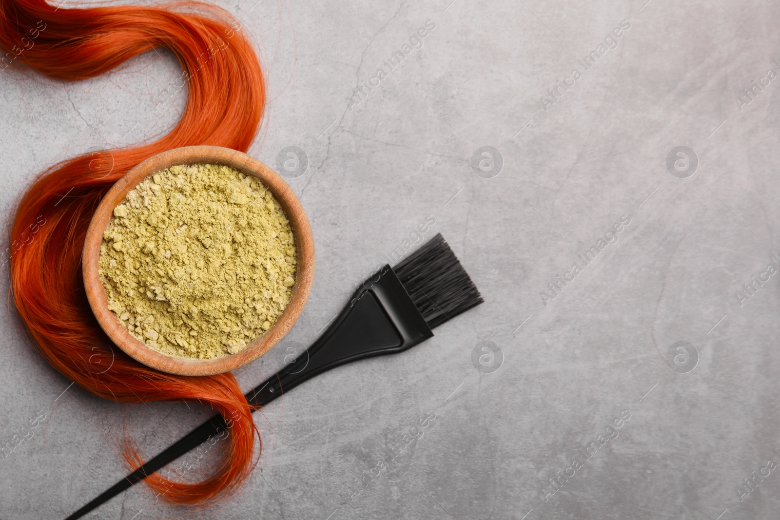 Photo of Henna powder, brush and red strand on grey table, flat lay with space for text. Natural hair coloring