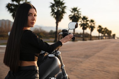 Beautiful young woman sitting on motorcycle at sunset. Space for text