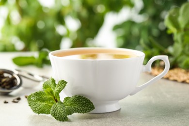 Photo of Cup of aromatic green tea with fresh mint on grey table against blurred background. Space for text
