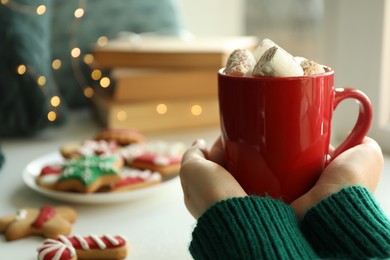 Photo of Woman holding cup of delicious hot cocoa with marshmallows indoors, closeup. Winter drink