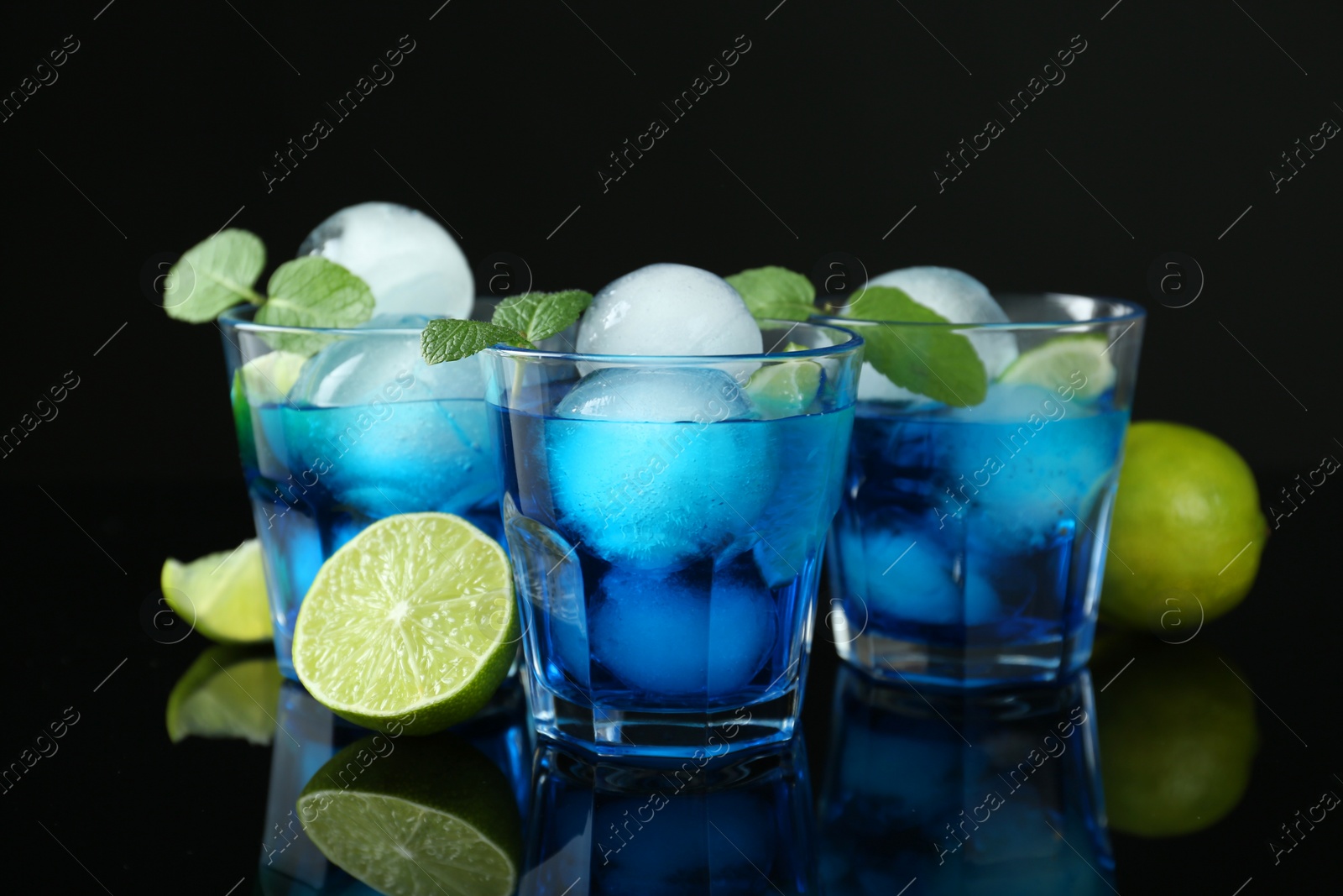 Photo of Delicious cocktails with ice balls, mint and lime on black background