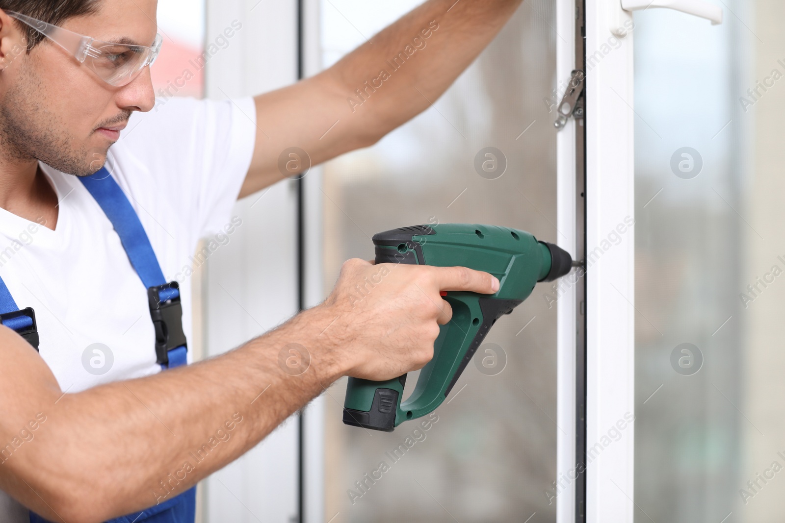 Photo of Construction worker repairing plastic window with electric screwdriver indoors