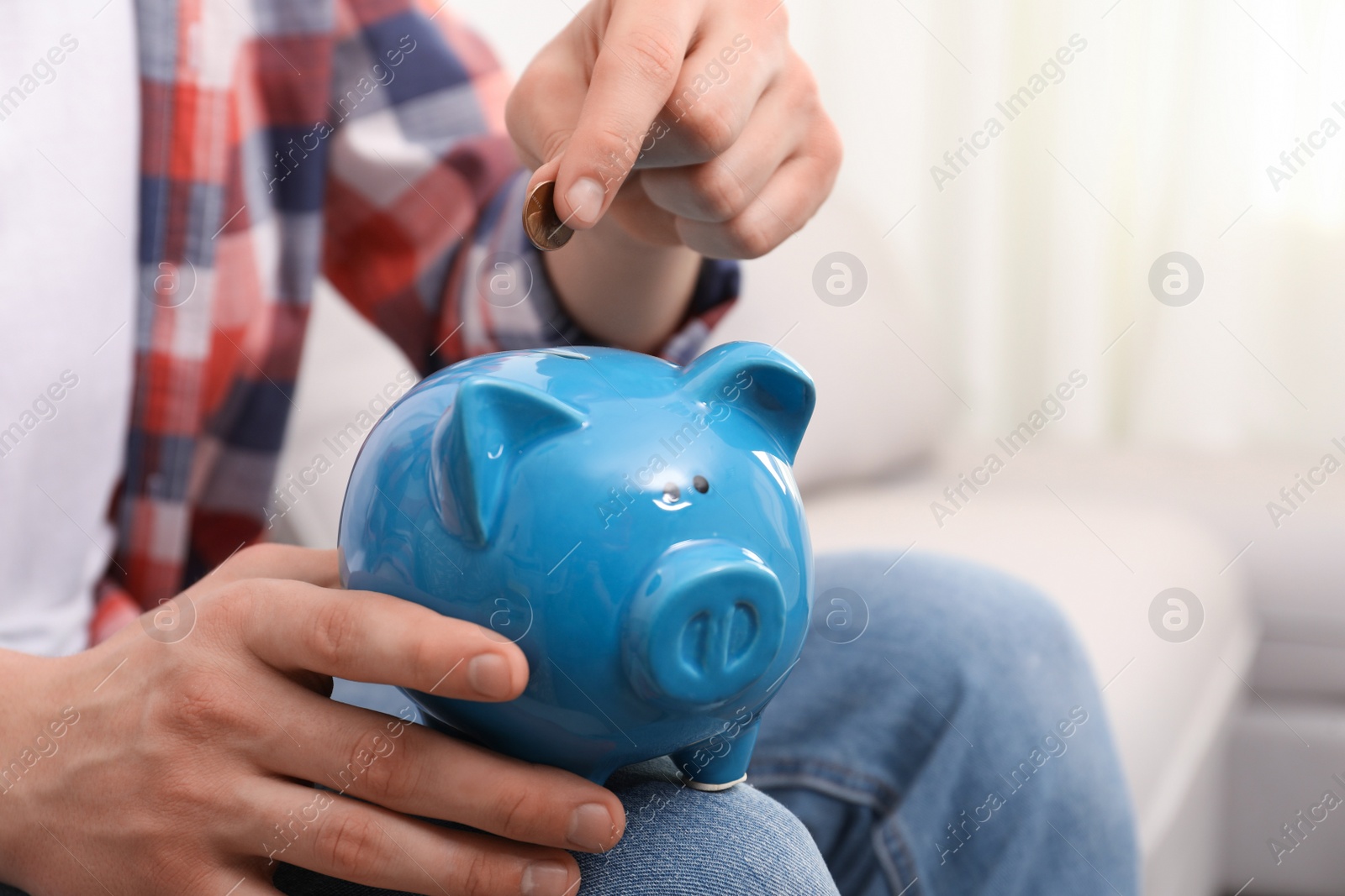 Photo of Man putting coin in piggy bank at home, closeup