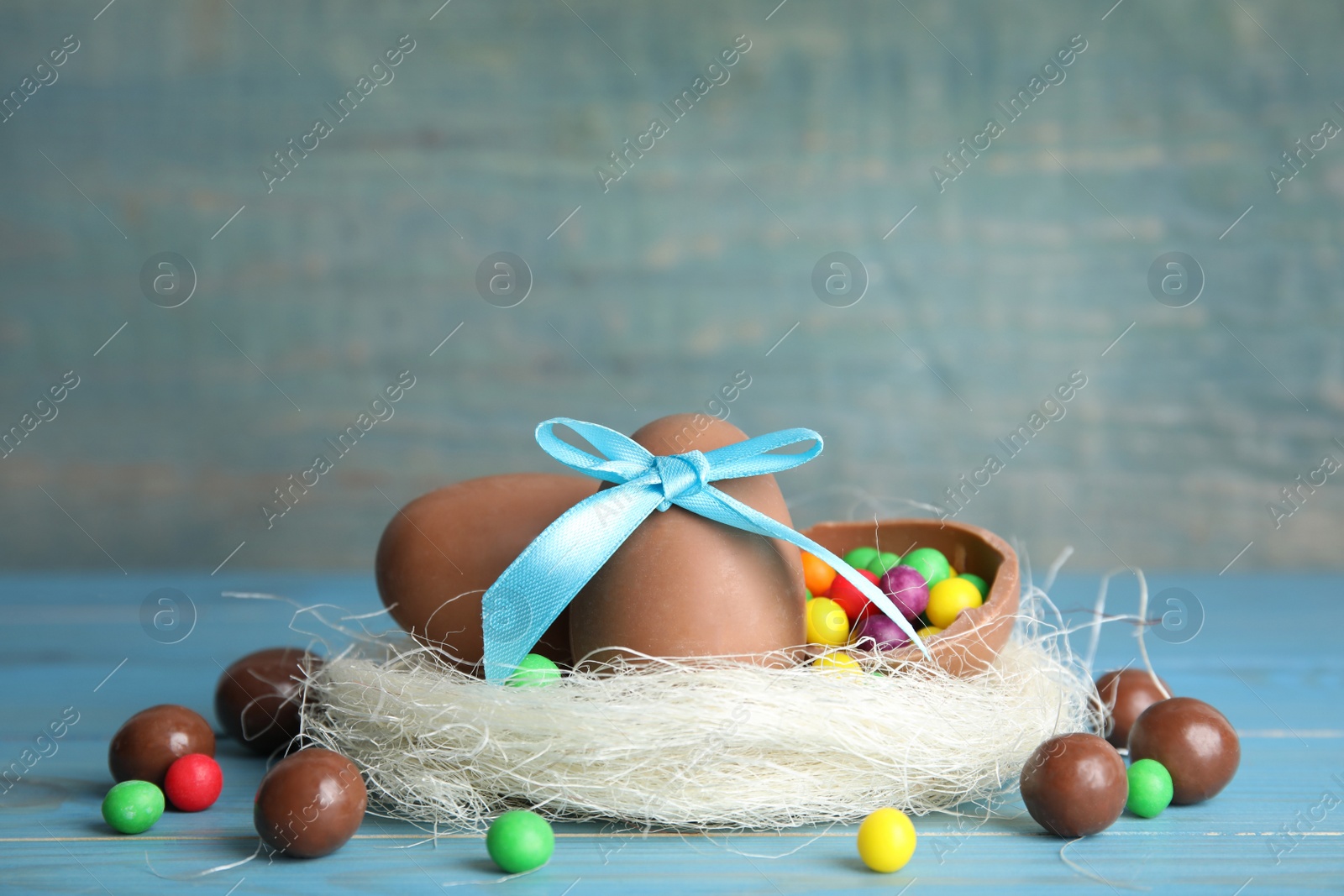 Photo of Composition with tasty chocolate eggs, colorful candies and decorative nest on light blue wooden table. Space for text