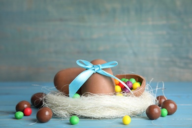 Photo of Composition with tasty chocolate eggs, colorful candies and decorative nest on light blue wooden table. Space for text