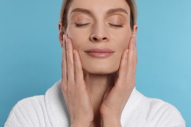 Photo of Woman massaging her face on turquoise background