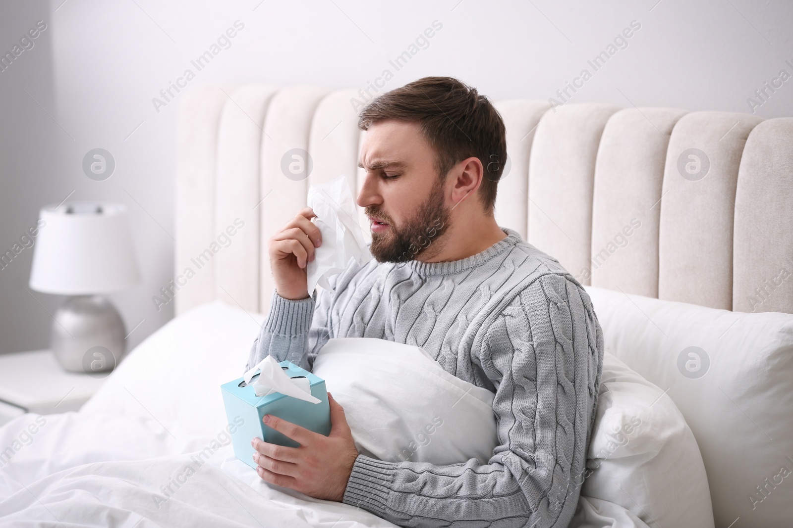 Photo of Young man suffering from runny nose in bed indoors