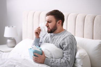 Photo of Young man suffering from runny nose in bed indoors