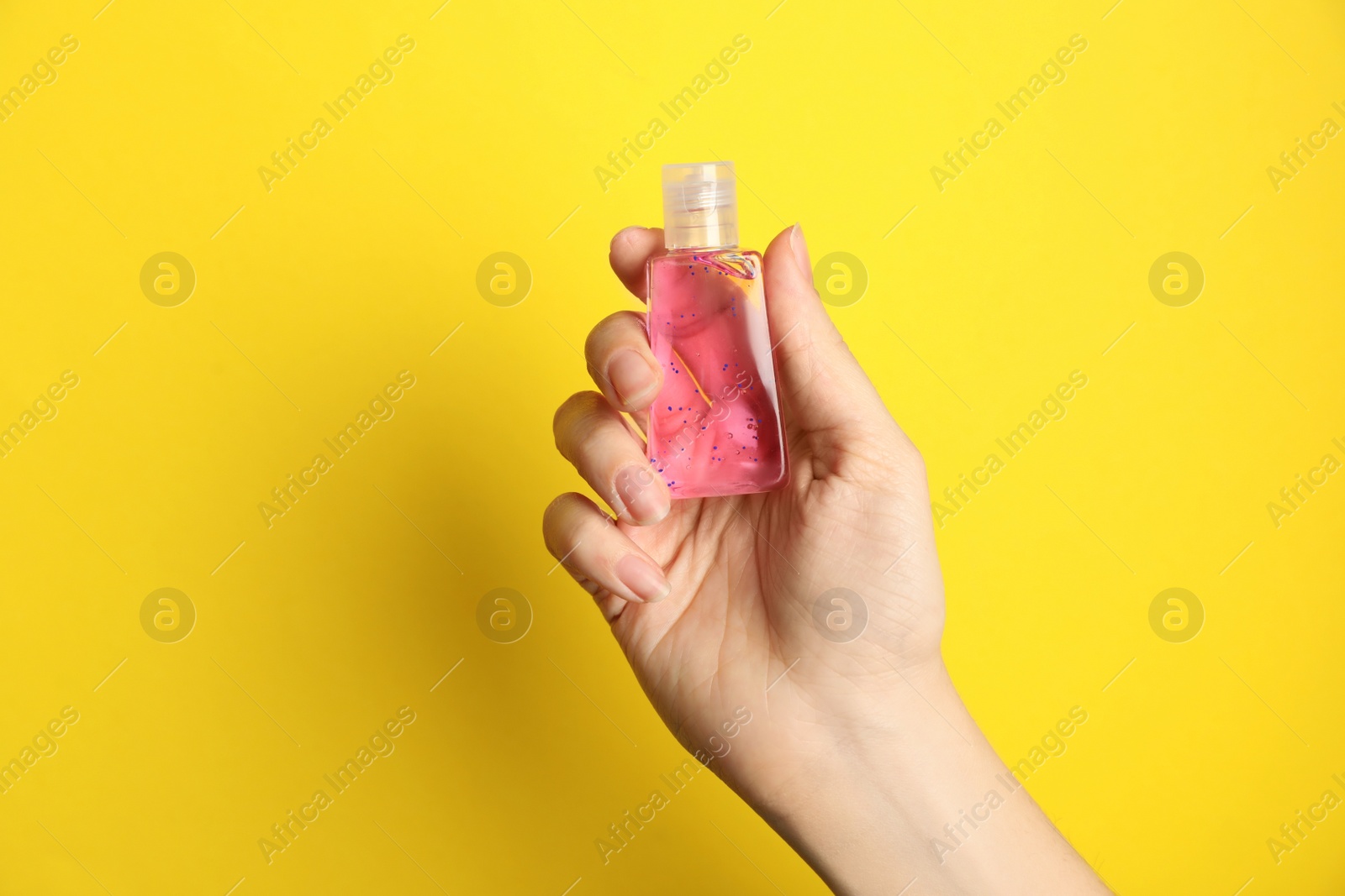 Photo of Woman holding antiseptic gel on yellow background, closeup