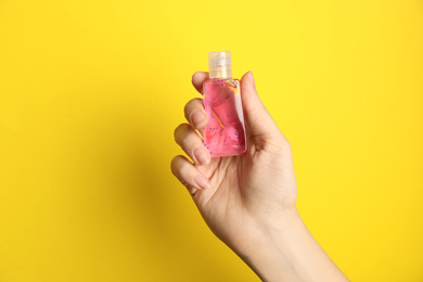 Woman holding antiseptic gel on yellow background, closeup