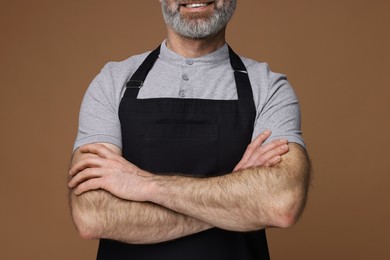 Man wearing kitchen apron on brown background, closeup. Mockup for design