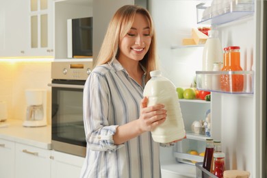 Photo of Young woman with gallon of milk near refrigerator in kitchen