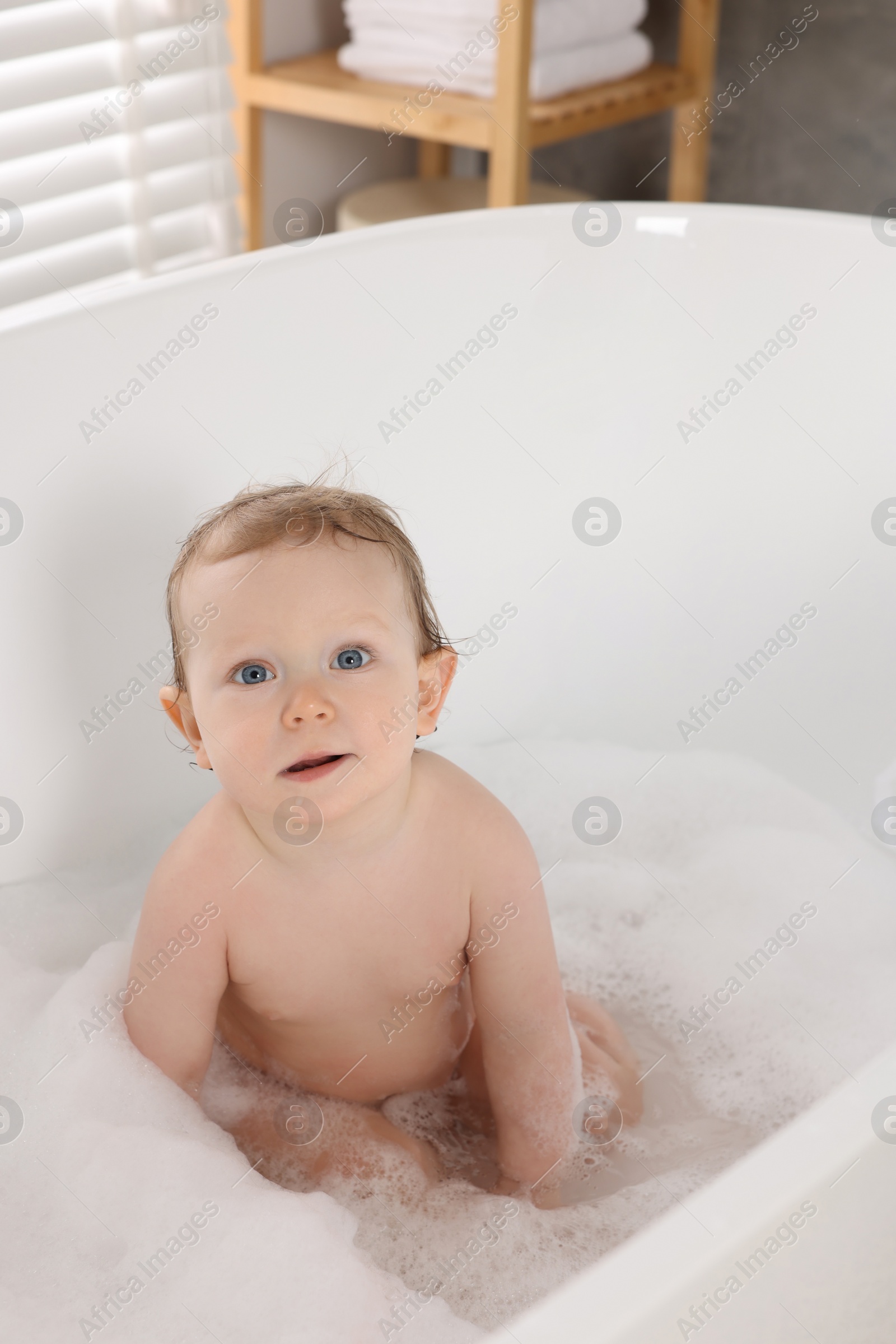 Photo of Cute little baby taking foamy bath at home