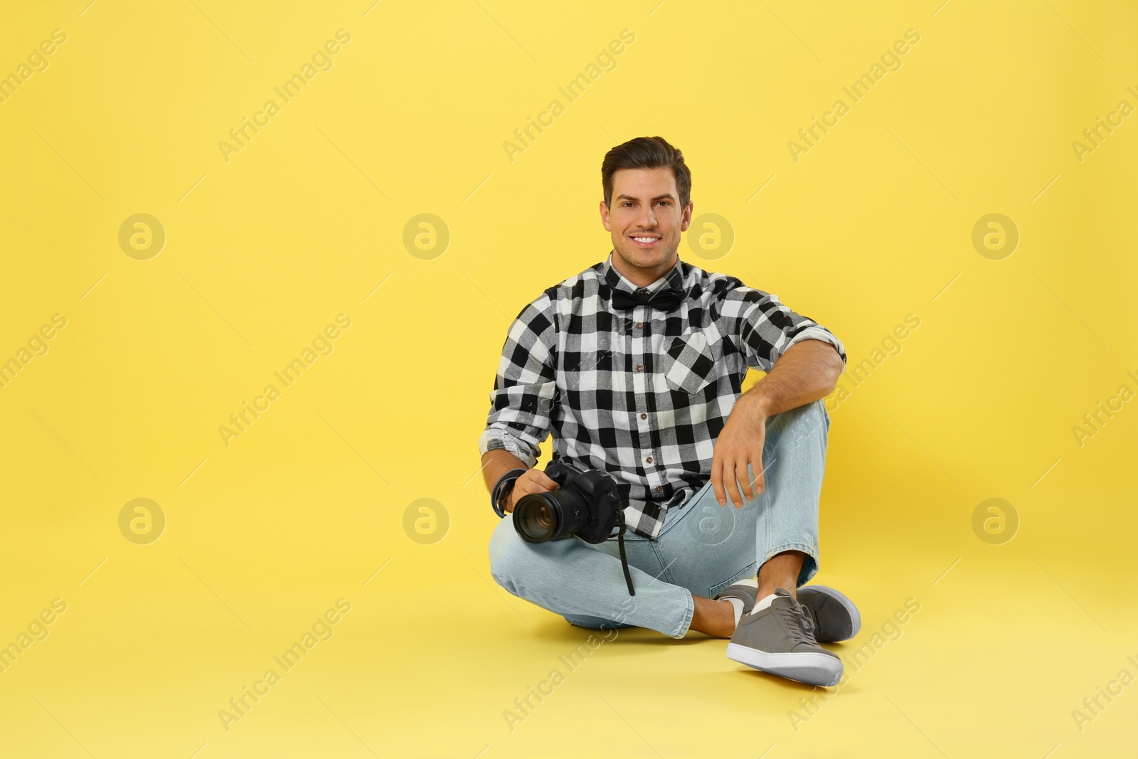 Photo of Professional photographer working on yellow background in studio. Space for text