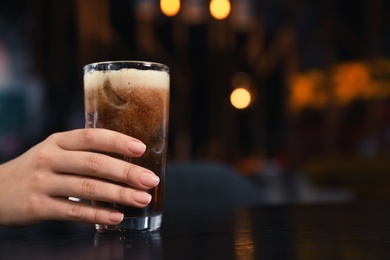 Woman with glass of refreshing cola at table indoors, closeup. Space for text