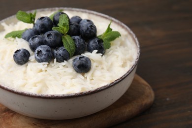 Photo of Bowl of delicious rice porridge with blueberries and mint on table, closeup