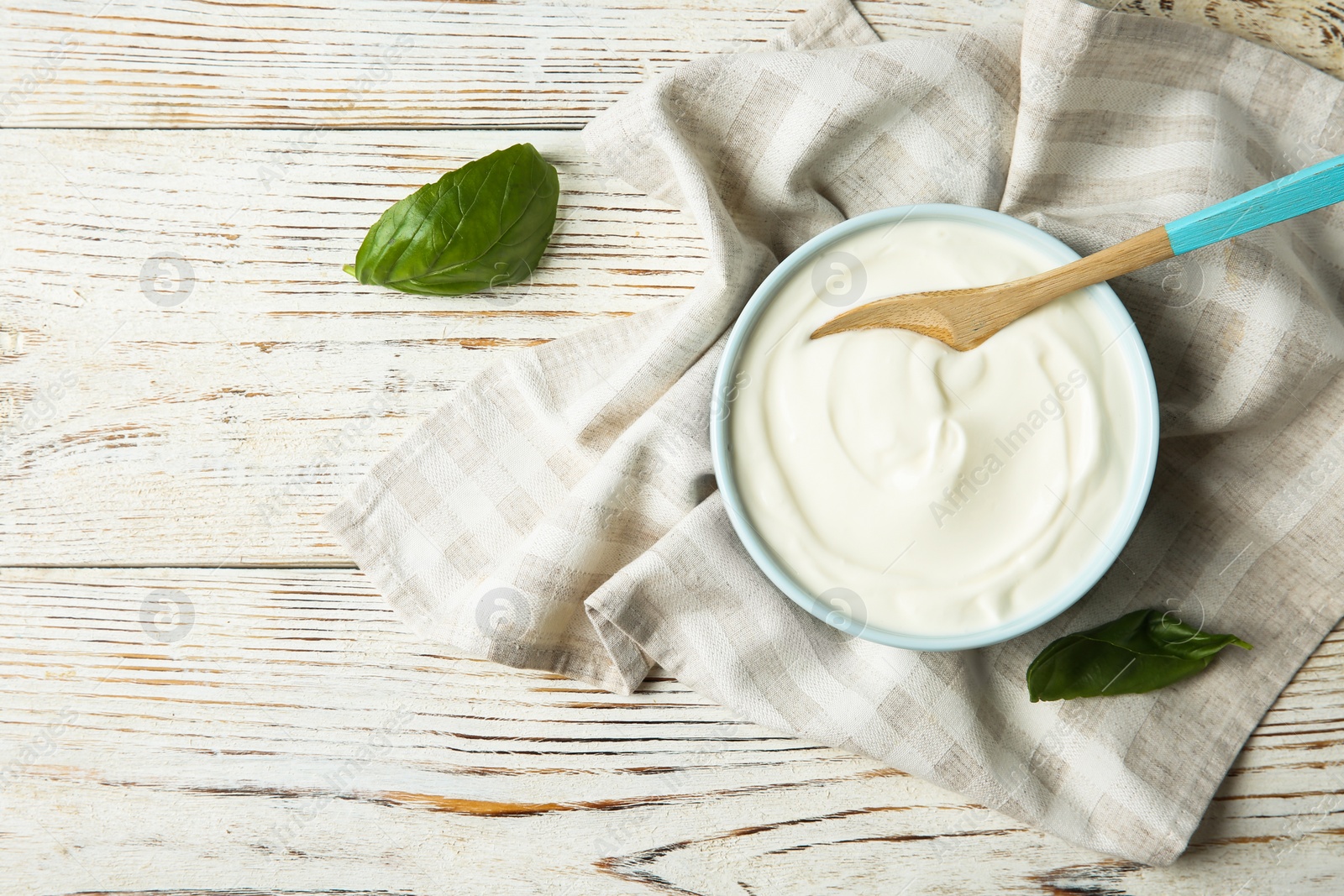 Photo of Bowl of sour cream with spoon and napkin on white wooden table, flat lay. Space for text