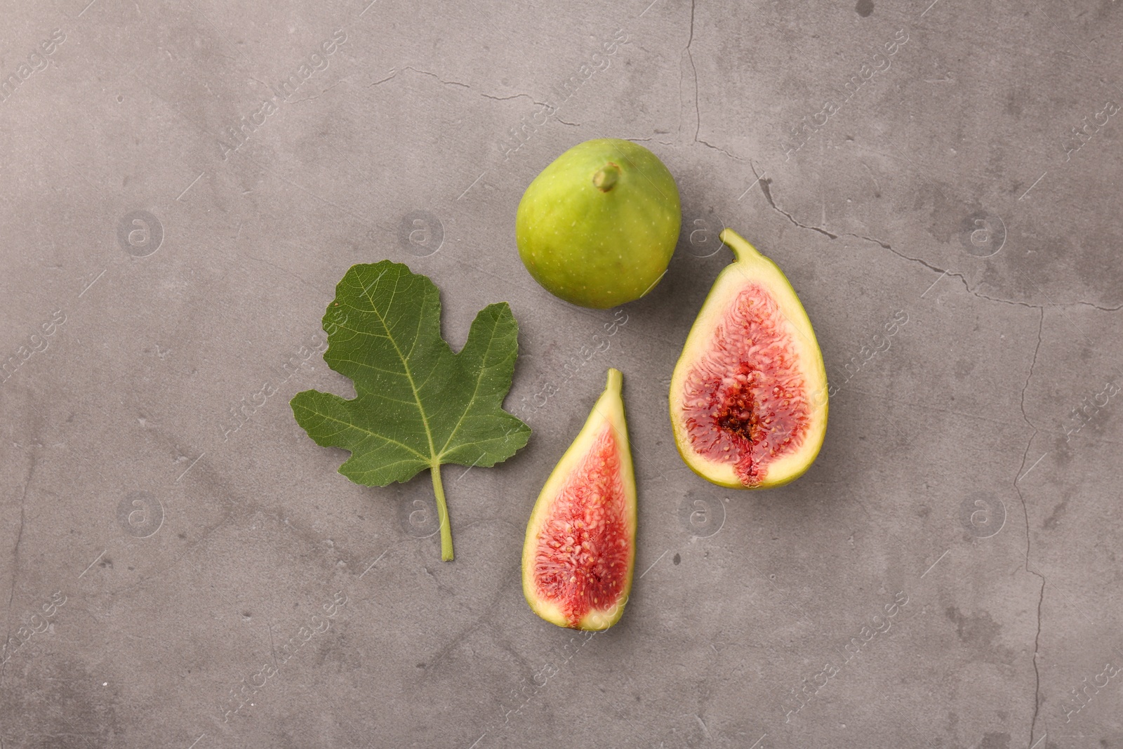 Photo of Cut and whole green figs with leaf on light gray table, flat lay