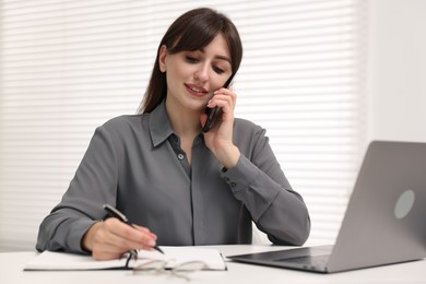 Photo of Smiling secretary talking by smartphone at table in office