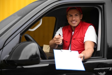Photo of Courier giving clipboard with documents out of car window outdoors