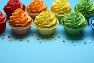 Photo of Many tasty cupcakes with bright cream and sprinkles on light blue background. Space for text