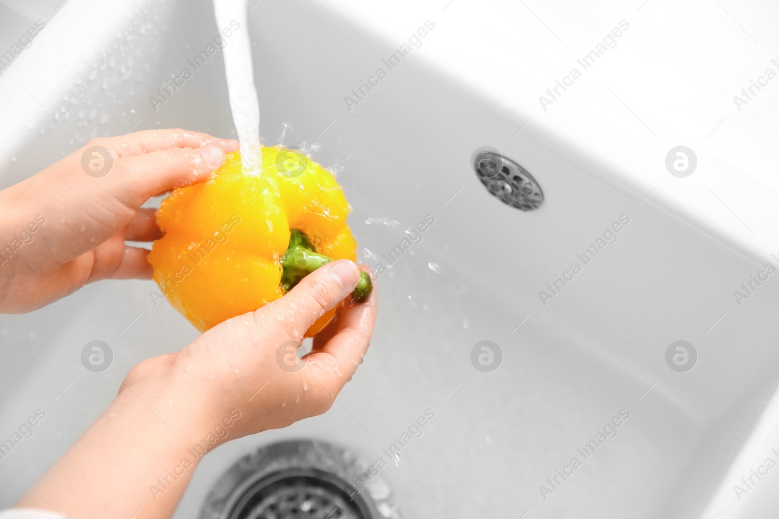 Photo of Woman washing fresh yellow bell pepper in kitchen sink, closeup. Space for text