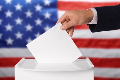 Election in USA. Man putting his vote into ballot box against national flag of United States, closeup