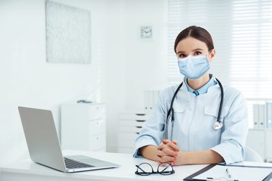 Image of Young doctor wearing medical mask at desk in office