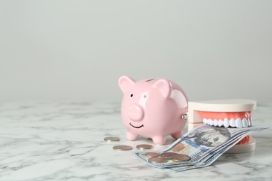 Photo of Educational dental typodont model, piggy bank and money on white marble table, space for text. Expensive treatment