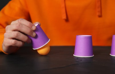 Photo of Shell game. Man showing ball under cup at black table, closeup