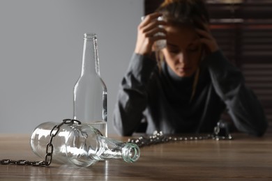 Photo of Alcohol addiction. Woman with glass of vodka at wooden table in room, focus on empty bottle