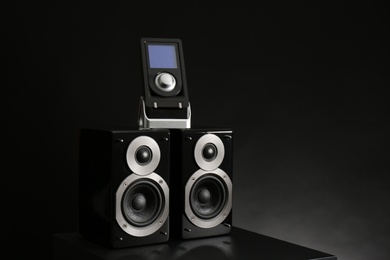 Photo of Modern powerful audio speakers with remote on table against black background. Space for text