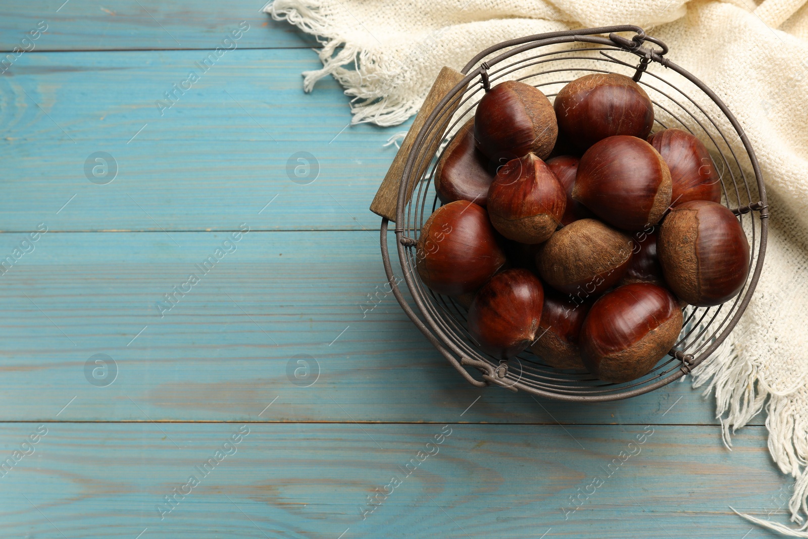 Photo of Roasted edible sweet chestnuts in metal basket on light blue wooden table, top view. Space for text