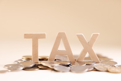 Photo of Word Tax made of wooden letters and coins on beige background