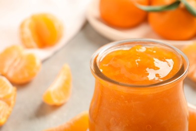 Photo of Tasty tangerine jam in glass jar on table, closeup. Space for text