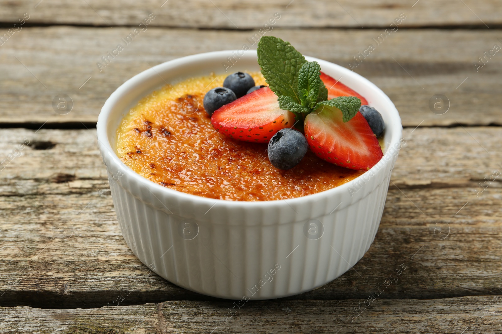 Photo of Delicious creme brulee with berries and mint in bowl on wooden table, closeup