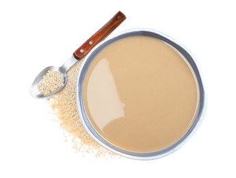 Photo of Tasty sesame paste in bowl, spoon and seeds on white background, top view