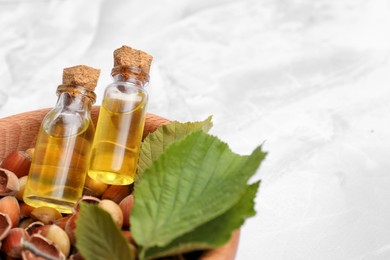 Bottles of hazelnut essential oil and nuts in wooden bowl on white table, closeup. Space for text