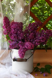 Photo of Beautiful lilac flowers in milk can near window indoors