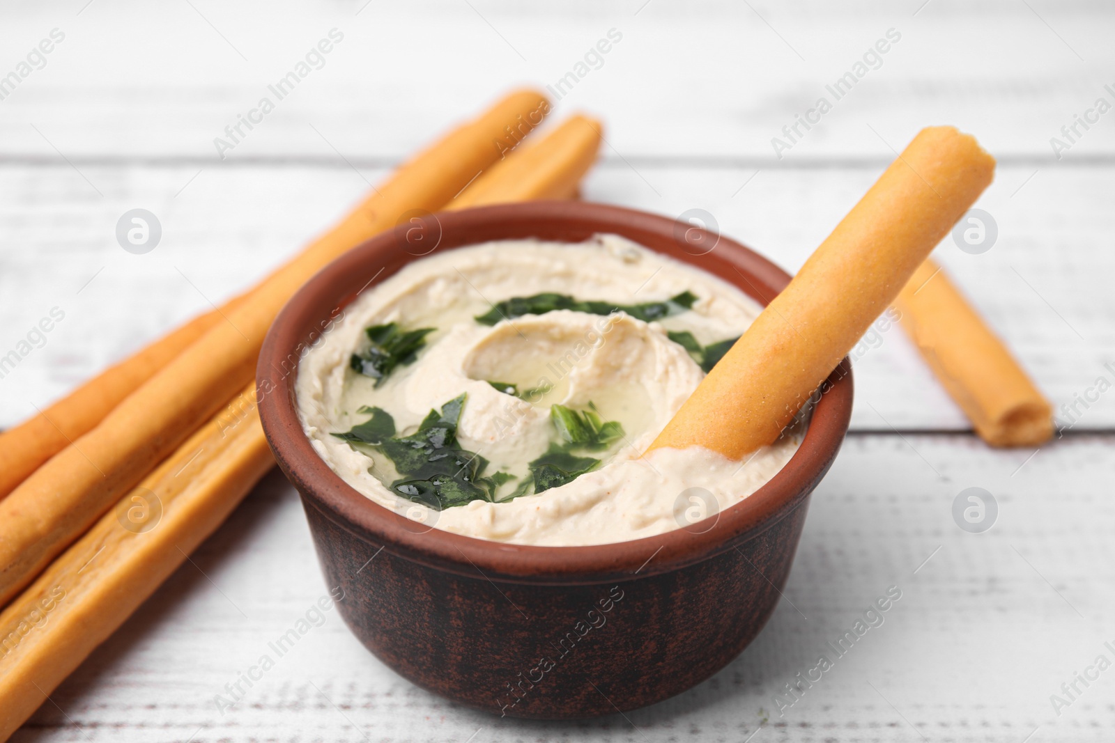 Photo of Delicious hummus with grissini sticks on white wooden table