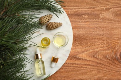 Pine essential oil, cones and branches on wooden table, flat lay. Space for text